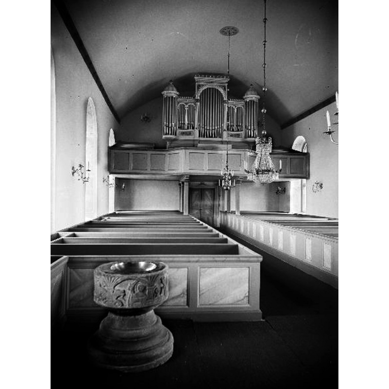 with the font visible in the foreground, at the east end of the south bank of pews -- Source caption: "Interiör mot väster. Efter restaurering."