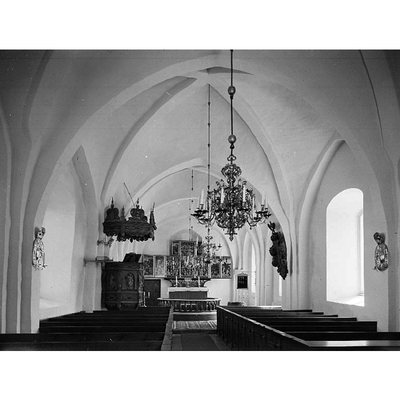 the top of the font is discernible behind the bank of pews, far [east] end, right [south] side