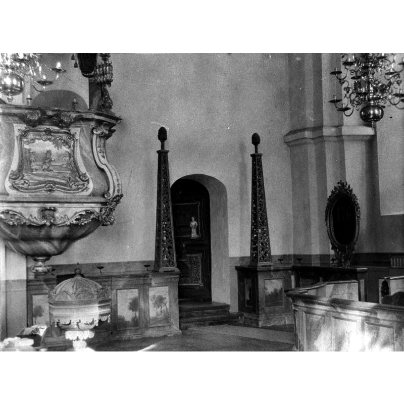 in the northeast corner of the church, beneath the pulpit, with the sacristy entranceway in the background