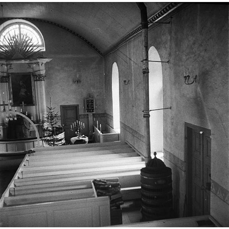 the interior as it was before the 1953 restoration; the font may be the object covered with a white cloth and supporting the candelabra, at the far [east] end, to the right [south] of the altar -- Source caption: "Interiör mot öster, långhusets södra del. Före restaureringen 1953."