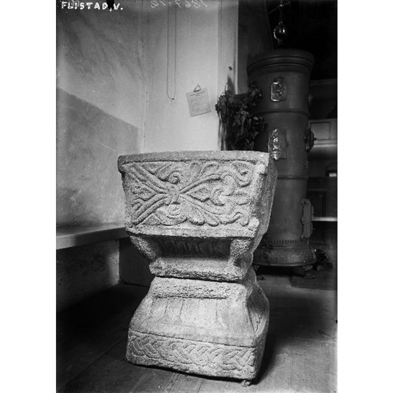 the old font seen here at the east end of the nave, south side, before the renovation -- Source caption: "Flistads kyrka [...] Dopfunt, sandsten, fyrsidig cuppa, från omkring 1200."
