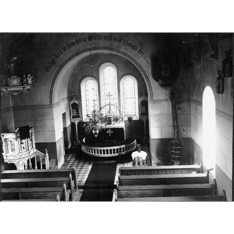 the interior of the new church; the font is visble, covered with a white cloth, near the heating stove, in the southeast corner -- Source caption: "Suntaks [nya] kyrka [...] Interiör mot öster, från läktaren."