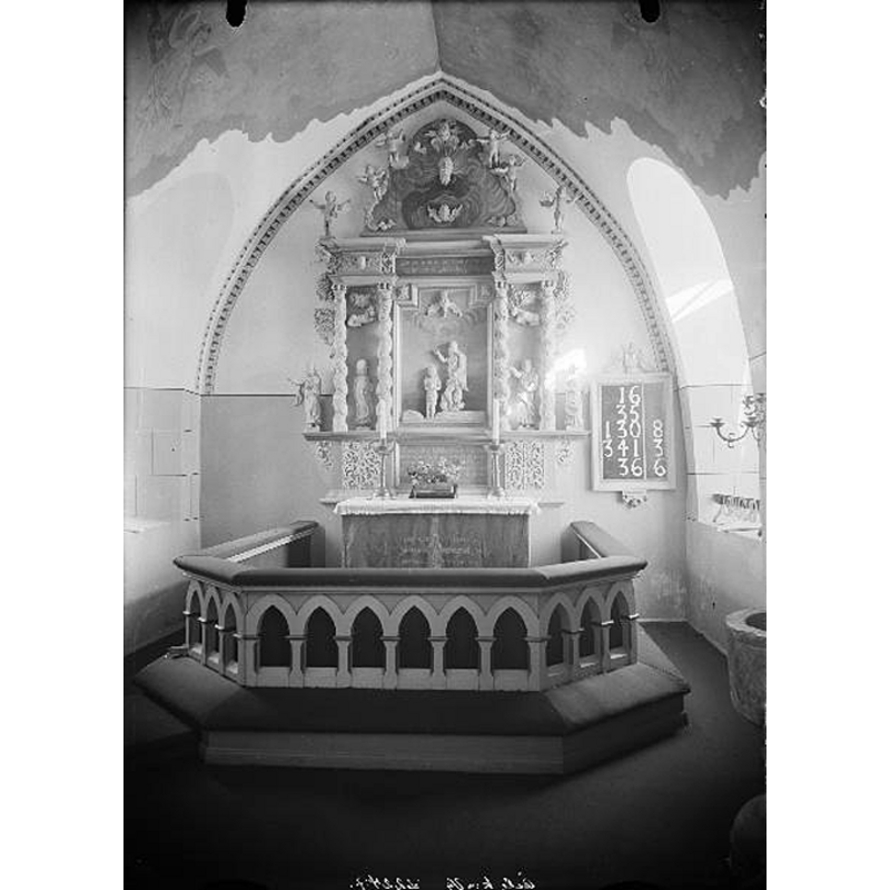 Source caption; "Åsle kyrka [...] Altaruppsats, snidat i trä från 1734 av mäster Cransberg. Flera skulpturer inramar altartavlan med motivet Jesu dop." -- the medieval font is partially visible in the bottom-right corner of the image