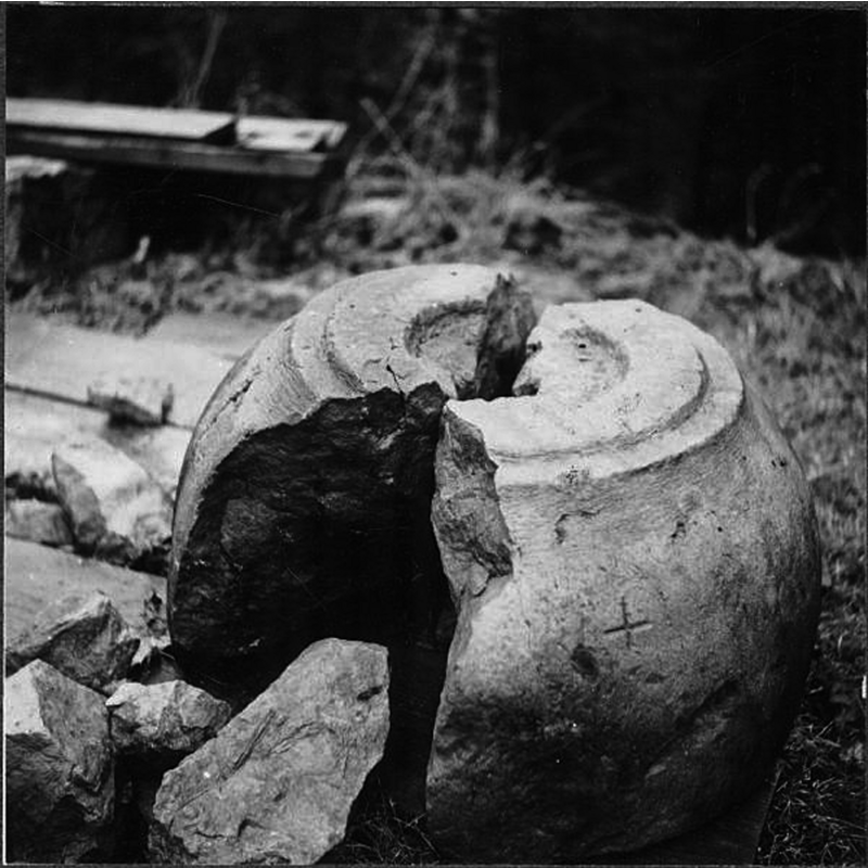 Source caption: "Toarps kyrka [...] Sten, möjligen dopfuntsfot, funnen vid schaktning på kyrkogården." -- according to Hallbäck (1966) the basin of a medieval font was recovered after more than a century of disuse in the churchyard and restored to the church in 1904; the base, however was discovered in a bog west of the church in 1942 and was restored to the church at a later date -- the image here shows the medieval base after its discovery,but the caption appears to contradict the details of its recovery as given by Hallbäck [cf. supra]