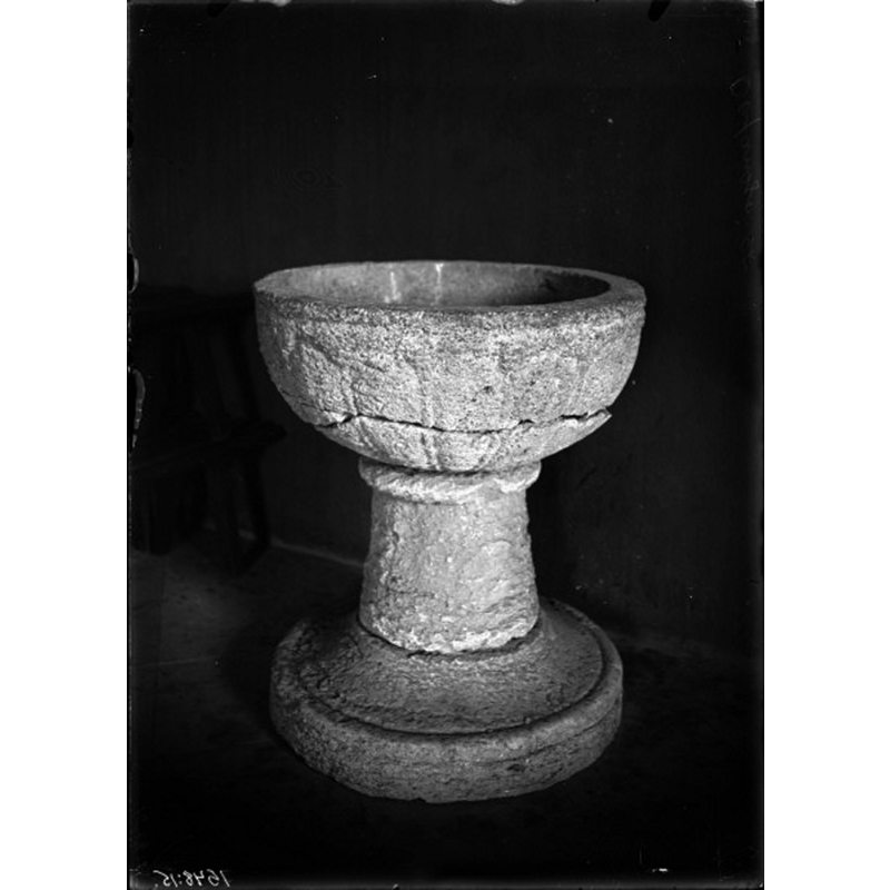 Source caption; "Ovansjö kyrka [...] Dopfunt av gulgrå kalksten av en känd gotländskt typ. Från 1200-talets mitt." -- showing the font damaged, disused, in the porch in 1917; the base appears to be made of two pieces (unless the lower base broke off)
