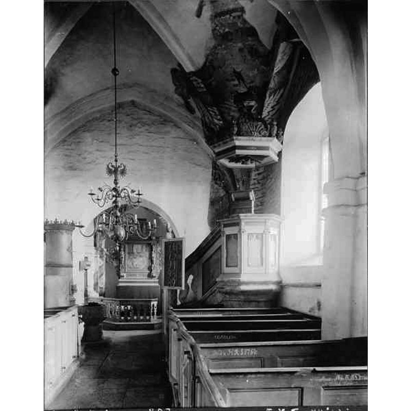 Source caption: "Hannas kyrka [...] Interiör mot öster." -- showing the medieval font at the east end of the centre aisle, near the old 'kakelugn'