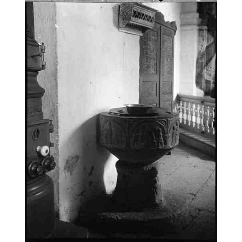 [NB: the source caption is mislabeled in the KMB entry] -- showing the medieval font against the north pillar of the chancel arch, near the old 'kakelugn' partly visible on the left