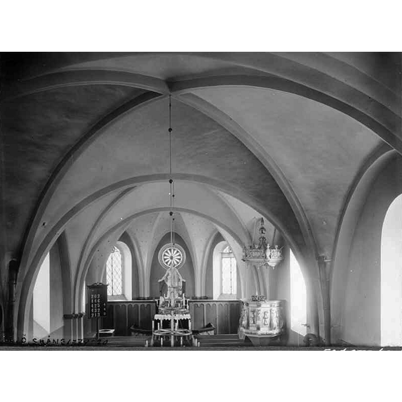 Source caption: "Össjö kyrka [...] Interiör mot öster. Foto från omkring 1910." -- showing the top of the font on the north side, to the left of the altar