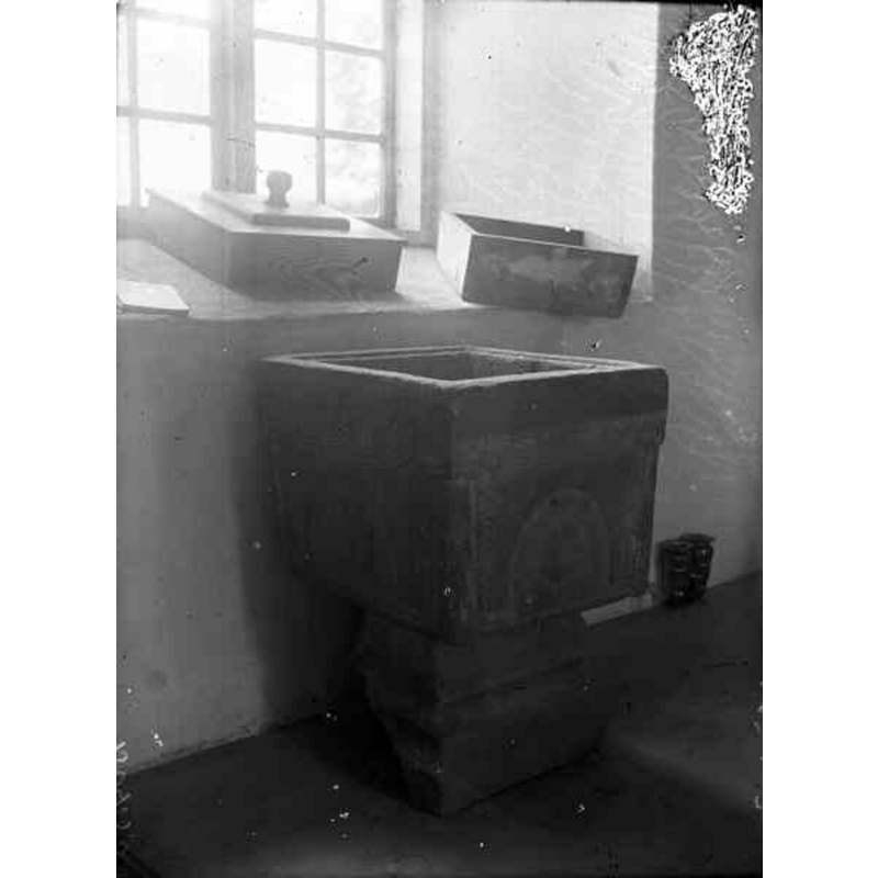 Source caption: "Nävlinge kyrka [...] Dopfunt av kalksten. Huggen palmettfris och rosetter. Spår av gul och röd färg." -- showing the font; its wooden cover shows on the window sill