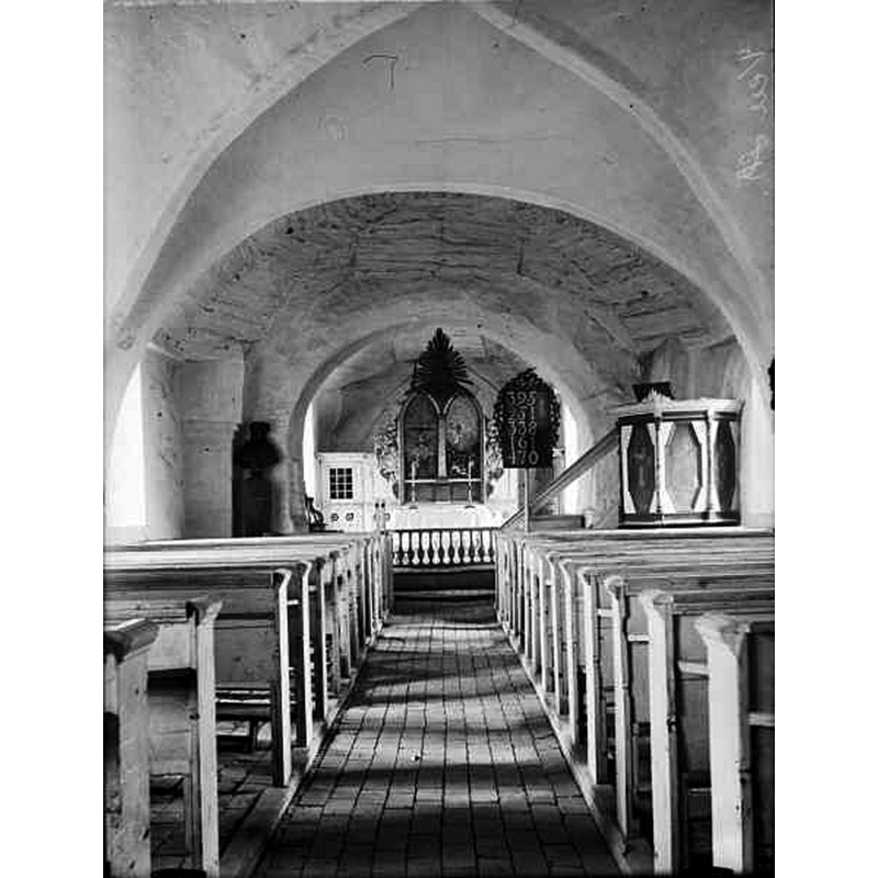 Source caption: "Sankt Ibbs gamla kyrka [...] Interiör mot öster." -- the top of the font cover can be seen semi-hidden at the back, left [north] side of the chancel arch