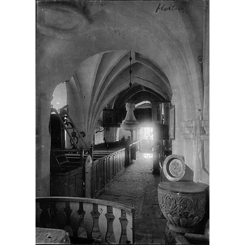 Source caption: "Vitaby kyrka [...] Kyrkan mot väster." -- showing the medieval font, its cover and baptismal dish by the right [north] pillar of the chancel arch