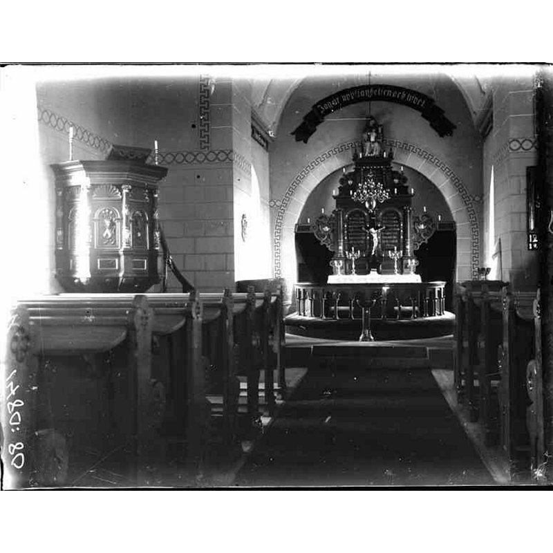 Source caption: "Östraby kyrka [...] Interiör mot öster." -- partially showing the medieval font, located on the left [north] side, between the pulpit and the communion railing