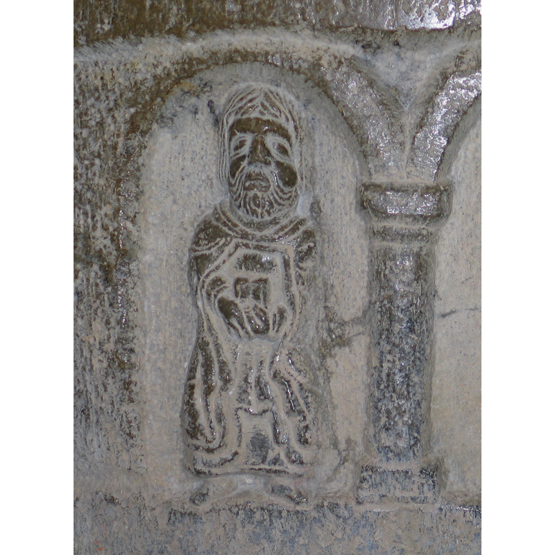 In the first arch from the right: a priest is clearly identifiable from his mantle; he holds a book to his middle with both hands