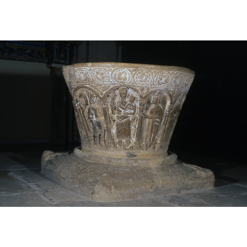 Adoration of the Magi. Under first arch to the far left, is a magi on horseback holding a gift in one hand. Under the second arch is a second Magi, on horseback, pointing toward the Madonna and Child. Under the third arch is a magi kneeling with a gift and you can see the head of his horse in the background. Under the fourth arch is the Madonna and Child. Under the fifth arch is Joseph who is standing holding the column with his right hand and a staff in his left hand