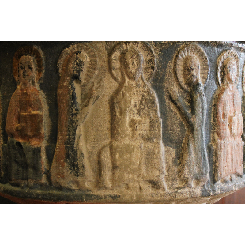 Christ in Majesty, sitting on a bench-like throne, haloed with cross. Right arm bent in benediction gesture, left arm holds a book over his knee. To the right and left, two figures in profile, hands together in prayer gesture, haloed. To the left six apostles, sitting, haloed, all holding a book on the left knee (open book). To the right six apostles, seated, also haloed and holding an open book on their left knee. The first figure to the right, has the right arm raised showing palm.