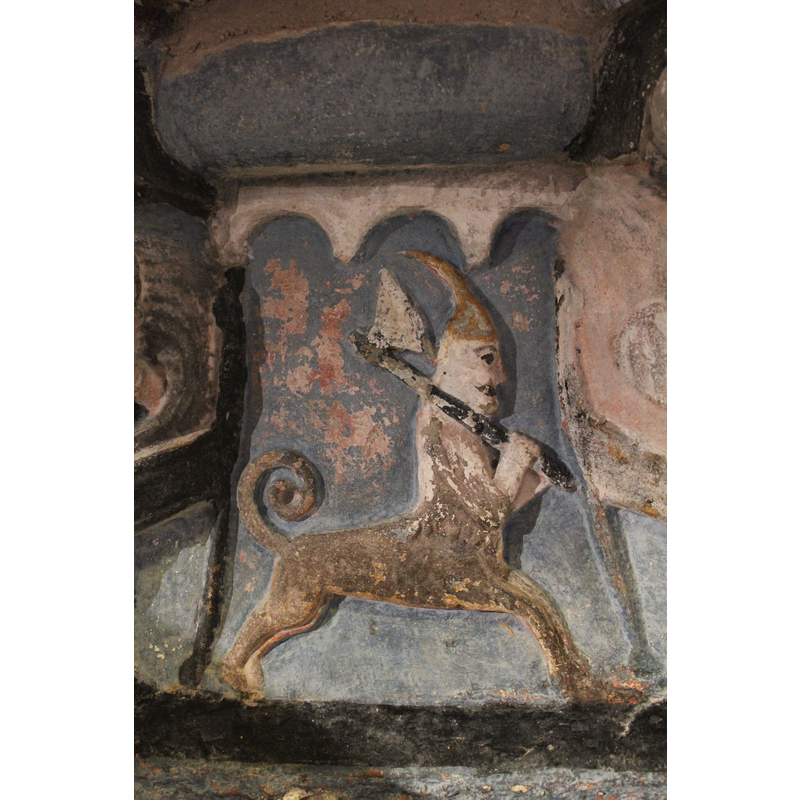 on the south side of the base; a centaur; the head wears a pointed, long hood and curved backwards, both hands hold a large axe over his right shoulder. The tail is long and coiled upwards