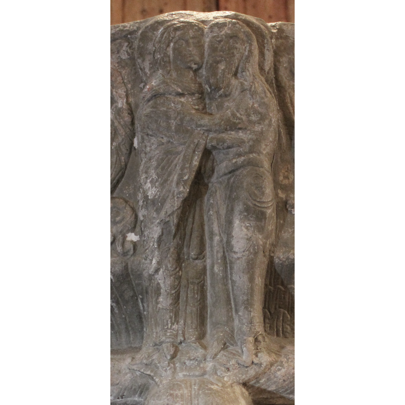 The two figures stand in profile and embrace. Both figures are haloed. Anna on the left wears long robes and a mantle. Her hair is exposed and has braids. Joachin is cheek-to-cheek with Anna and stands to her right. He has long hair past the shoulders, a mustache and a full beard. He has no head-cover. He wears a belt or sash. They stand on the heads of the two snakes whose jaws are interlocked.