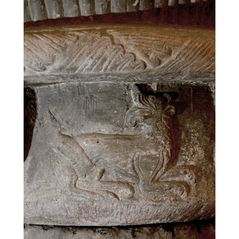 The lion is lying down looking backward with an open mouth and protruding tongue