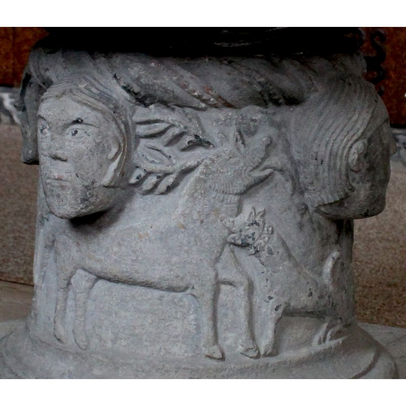 on the southeast side of the base; a stag faces right, head raised and antlers back, tongue out; it is being bitten on the neck by a hunting dog with a collar facing left.
