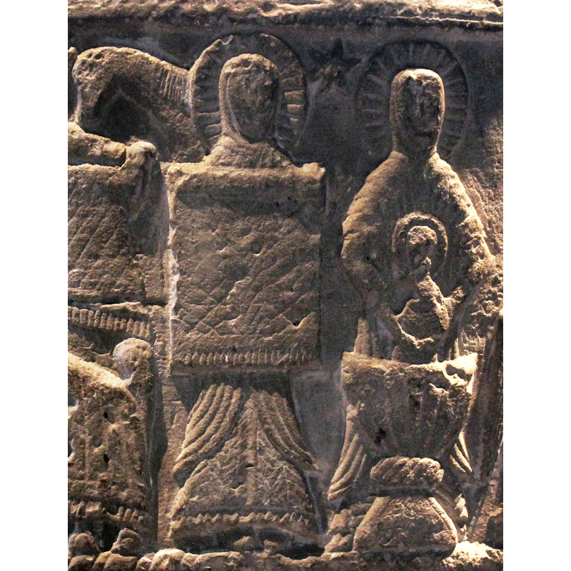 Christ's first bath; two figures in attendance, both haloed; the one on the left holds up rich blanket; six-point star above. Christ Child being held in a font.
