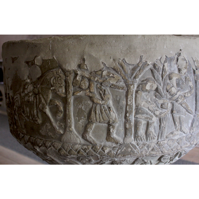 Two figures (under one arch). The figure on the left is smaller, 2/3 profile, head is bent forward, arms stretched forward holding a plant taller than he is (is this sheafs) - the right hand could be holding scythe. The person wears a short skirt and toes visible. The figure on the right is taller, full frontal, wears a coat of armour and helmet, the left arm bent at the elbow the scabber - the right arm bent at the elbow - the hand grabs the handle of the sword. He is posed in an action to remove the sword from scabber - the feet have shoes.
