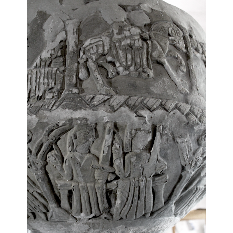 One arch, 3rd scene underbowl. Two figures both sitting down, full frontal, heads turned toward the right. Left arms bent at the elbow, raised with index fingers pointing upward, thumb inward. The left hands rest on the left knees - the poses are identical - and hold a sword pointing upward.