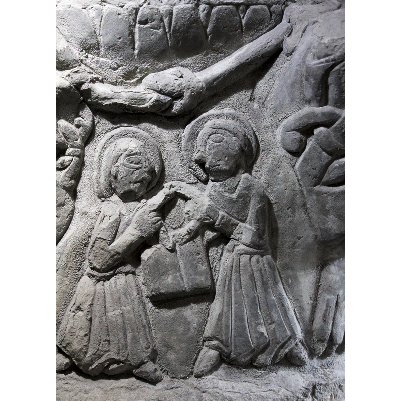 2nd scene of figures on the base. This has two figures, 2/3 profile, facing each other, haloed, The figure on the left has the right arm, bent at the elbow, and holds the left side of something circular (wreath?). The figure on the right in a similar position to the other one, the left arm that holds the wreath in a similar position. The right arm and left arm of the left hand figure, appear to be holding a book from behind and below the wreath. Both figures wear long robes and wear shoes. No crowns on either figure.