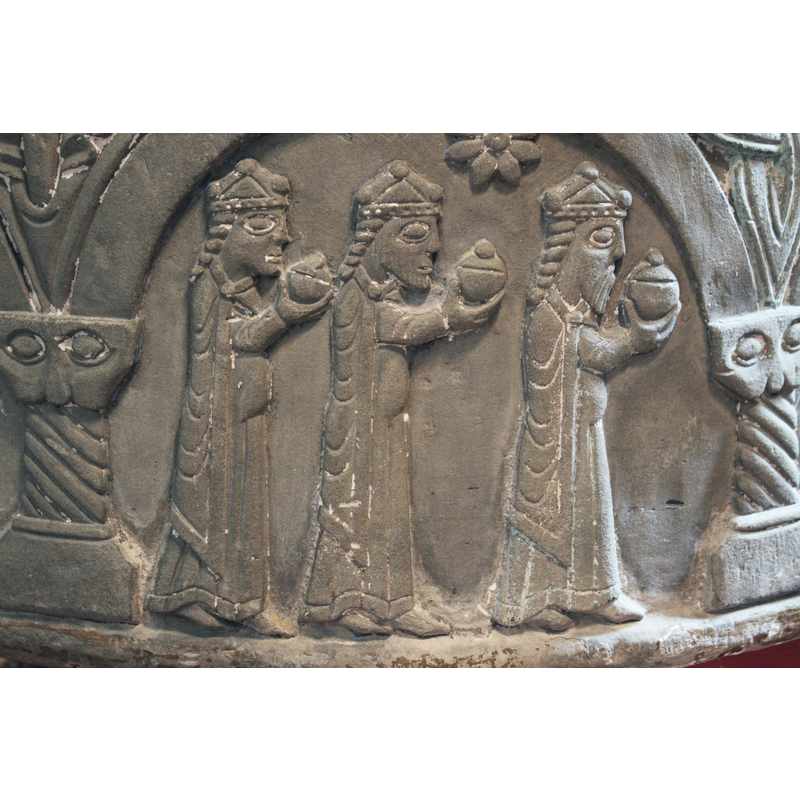 The scene of the Adoration of the Magi takes place under two arches. The first arch shows the three Magi walking in profile from left to right, wearing identical garments and three-knobbed crowns; they cary identical gifts. A star resembling an eight-petalled flower appears above the heads of the first two Magi. The scene continues in the next arch.