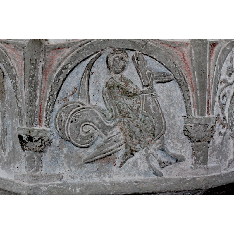 on the southeast side of the font [orientation is approximate] -- a human figure riding a fabulous beast passant, towards the right; the beast is not an aspis proper, having an ambiguous head [perhaps a reptile's?], an avian body (wings and two legs), and a double-coiled dragon's tail. Possible two fabulous beasts of somewhat similar form, beside the aspis: jaculus and scitalis. On oher Byzantios' fonts the rider usually mounts a beast closer in form to an aspis