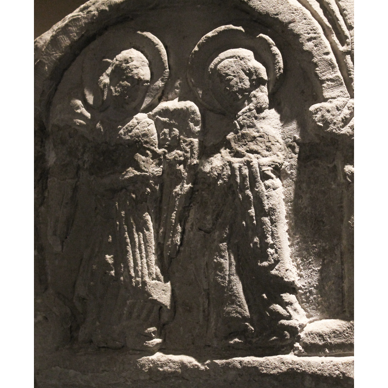 Two figures, to the right is the Virgin, in profile, head is haloed, with head covered, left hand raised toward the angel. Mary wears a mantle and long robes; her head is bent slightly forward. To the left is the angel, haloed, full front pose, head looks 2/3 towards Mary, both wings open and visible, the right hand points to Mary, the hand is worn or broken; the left hand of the angel shows out from under the mantle and holds it against the body. No stars, doves, etc.