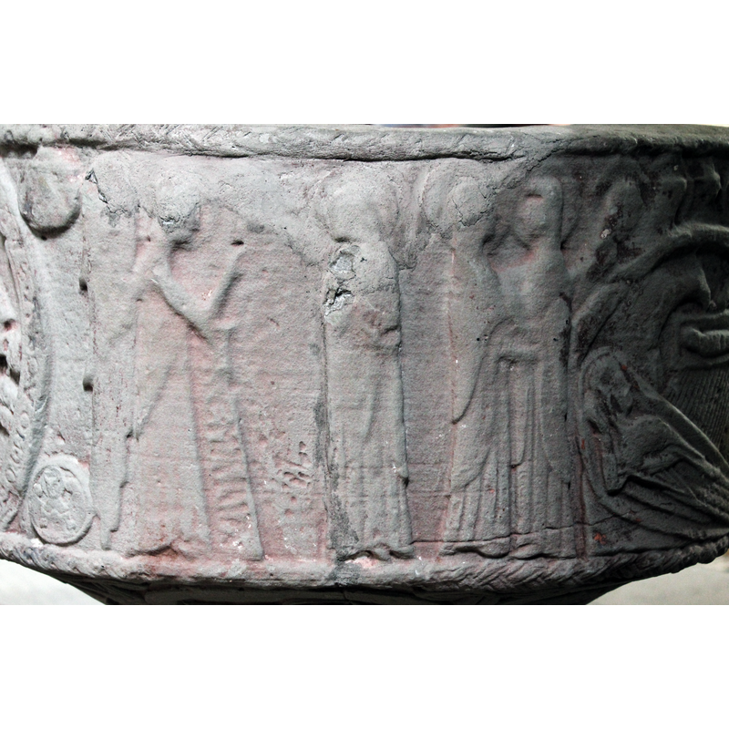 on the southwest of the basin [orientation is approximate] -- Two figures in profile, to the left is the angel with wing full length of body; the angel faces Mary and raises its right hand, the finger is pointing diagonally upward; there is a long-stemmed object (lectern? scroll? banner?) in front of the angel with an inscription on it:, "AVE MARIA". On the right is Mary, haloed, facing left, head downward, the arms apparently close to the body, but there is damage to the stone in that area; Mary wears a mantle over her gown. [NB: the upper part of this side was broken and has been repaired; unknown whether the repair was made with the original triangular piece that broke off].