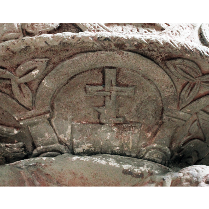 on the west side of the underbowl [orientation is approximate] [NB: this side, which includes the Majestas Domini on the basin side, and the Etimasia on the underbowl, may have faced east in the original orientation of the font before its relocation within the church] -- Etimasia in one of the seven arches of the underbowl: a dove facing left and a cross, th e arms of the cross interwoven at the centre point, on an altar. Triquetra motifs in the spandrels