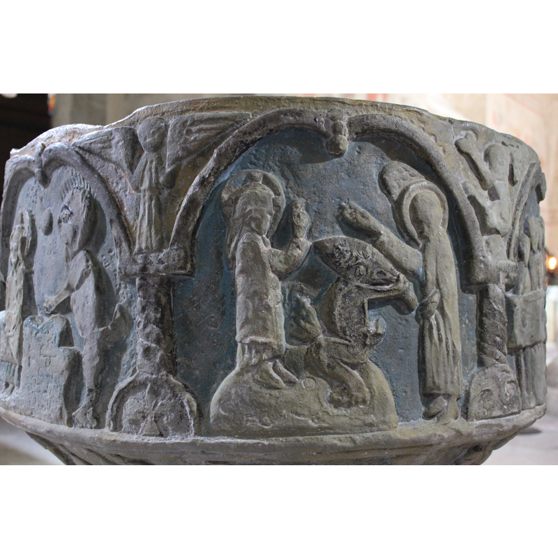 Three figures inside this arche, the one on the left, Christ, stands on a rock in profile; he is cross-haloed and has long hair; the right hand is raised in benediction, the left hand holds a mantle across his waist. Seated on the same rock, to the right is a devil-like figure; its face is twisted horizontally, parallel to the ground, and is pulling on his hair; the body is animal-like, with a tail. The haloed figure on the right stands in profile, a wing showing above his head, an angel;  the ight hand raised diagonally and pointing across (upward to the heavens?); the left hand holds a mantle. In the spandrel to the right a four legged animal in a vertical position.