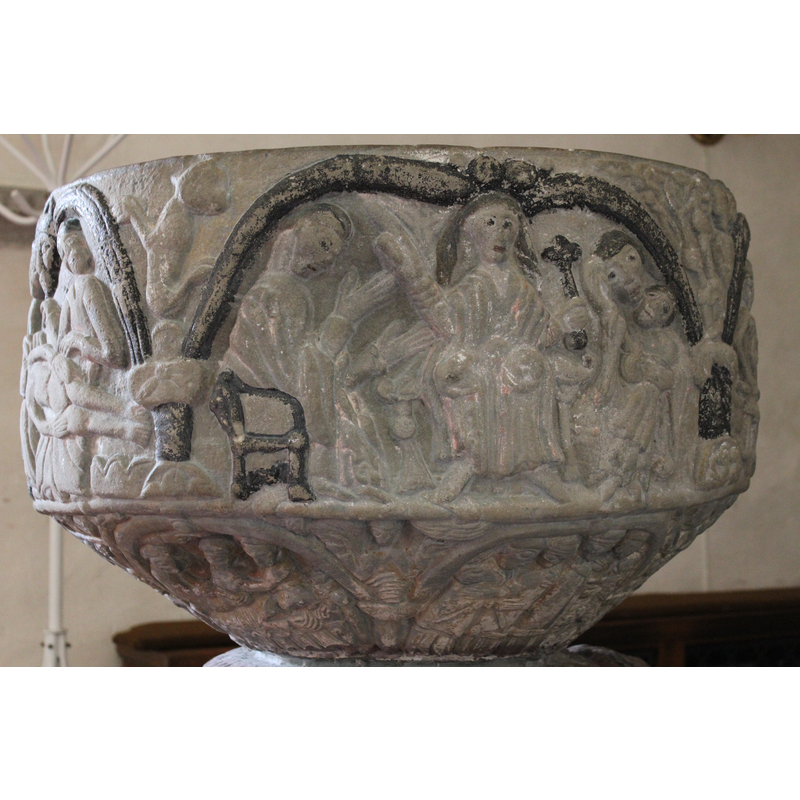 In the centre is Christ in Majesty [NB: SK: Gotland identifies as a possible Sermon on the Mount]. Holding a cross, long hair, right arm and gesture of benediction. Left arm bent at elbow and holds the cross. To the right, is the Madonna and Child. Madonna is seated. She hold a child in her left arm, child sits diagonally, her right hand supports her head which is inclined. To the left of Christ is a seated figure which is in profile, head slightly bent forward. Right arm bent at elbow at 45* angle and palms stretched - gesture of adoration or praise. Left arm  and palm outward. Sermon on the Mount? According to Roosval. In the spandrel - a four legged animal.