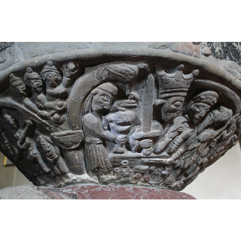 UNDERSIDE SCENE NUMBER 1 (MOVING FROM RIGHT TO LEFT)  The scene (under one arch) has four figures. The figure to the right is dressed in animal skins He wears a hat and bearded and his head faces upward. (lies sidewys). It appears to be St.John the Baptist  preaching. To his left is a woman's figure, full frontal, she wears a headcovering with ornaments, her left hand rests on the table, holding a large knife. The right arm rises vertially up and her hand is bent and pointing the finger to St.John. Is she Herodias as Roosval suggests? To the left is a king crowned, looking toward the scene of woman and St.John. His right arm holds a sword pointing up. The left arm is up and the hand points a finger to St.John (across his neck the finger is held). King Herod. To the left stands a man in profile he right arm extended forward and holds a large chalice the left hand raised above it- and above this man there is a dove. (Stephan and the cock - accorrding to Roosval).IN THE SPANDREL Three men wearing all the same hats, holding stones, to stone stephan who was the first martyr.