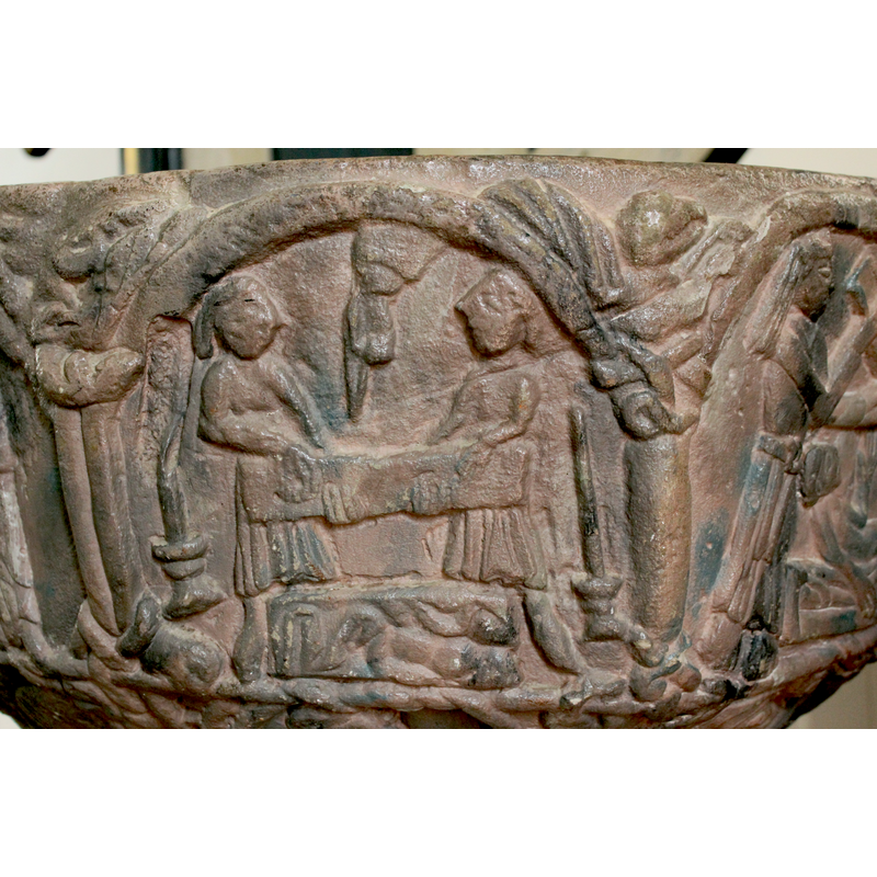on the north side of the basin [orientation is approximate] -- At the bottom of the composition, there is a rectangular box with some cloths; behind it stand two male figures (they are bearded) holding another rectangular object, the cover of the sarcophagus, the figures holding the lid with both hands. From above the Hand of God and points a long finger toward the sarcophagus in a typical Hegvald gesture. A large candle in a moulded candle-holder stands on either side of the scene