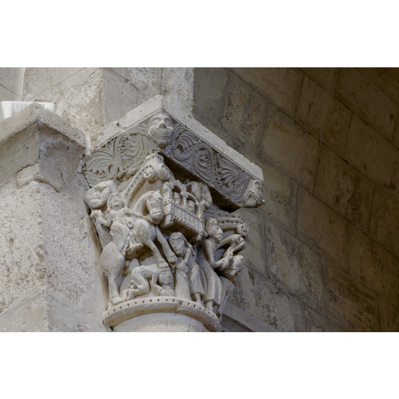 capital on the north side of the chancel arch: on the left side of the capital is a mounted male holding an object and/with a flowing cloth in the right hand; the left hand hold the bridle and a ring, or the ring is secured to the saddle; the horse tramples over a fallen bearded man who appears unarmed; the front side of the capital has a balcony with two males in it looking out; below the balcony a male figure leans on a short pillar (to which he may be tied?); the right side of the capital has a bearded man loading a stone into his sling, by the side of a mounted knight armed with a lance and a shield, and wearing a helmet; behind him is an unidentified beast