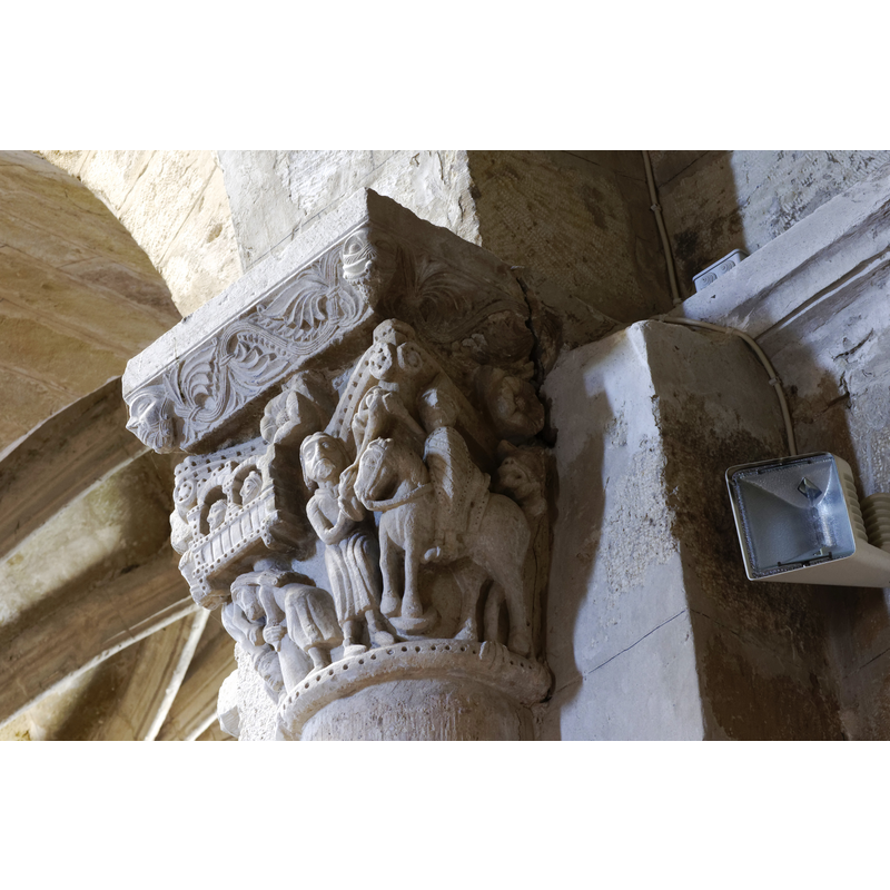 capital on the north side of the chancel arch: on the left side of the capital is a mounted male holding an object and/with a flowing cloth in the right hand; the left hand hold the bridle and a ring, or the ring is secured to the saddle; the horse tramples over a fallen bearded man who appears unarmed; the front side of the capital has a balcony with two males in it looking out; below the balcony a male figure leans on a short pillar (to which he may be tied?); the right side of the capital has a bearded man loading a stone into his sling, by the side of a mounted knight armed with a lance and a shield, and wearing a helmet; behind him is an unidentified beast