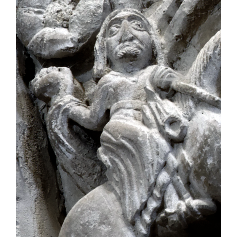 capital on the north side of the chancel arch: on the left side of the capital is a mounted male holding an object and/with a flowing cloth in the right hand; the left hand hold the bridle and a ring, or the ring is secured to the saddle; the horse tramples over a fallen bearded man who appears unarmed; the front side of the capital has a balcony with two males in it looking out; below the balcony a male figure leans on a short pillar (to which he may be tied?); the right side of the capital has a bearded man loading a stone into his sling, by the side of a mounted knight armed with a lance and a shield, and wearing a helmet; behind him is an unidentified beast