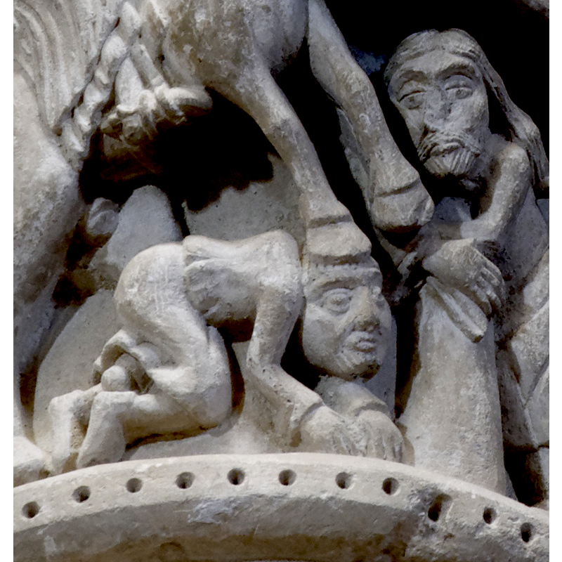 capital on the north side of the chancel arch: on the left side of the capital is a mounted male holding an object and/with a flowing cloth in the right hand; the left hand hold the bridle and a ring, or the ring is secured to the saddle; the horse tramples over a fallen bearded man who appears unarmed; the front side of the capital has a balcony with two males in it looking out; below the balcony a male figure leans on a short pillar (to which he may be tied?); the right side of the capital has a bearded man loading a stone into his sling, by the side of a mounted knight armed with a lance and a shield, and wearing a helmet; behind him is an unidentified beast