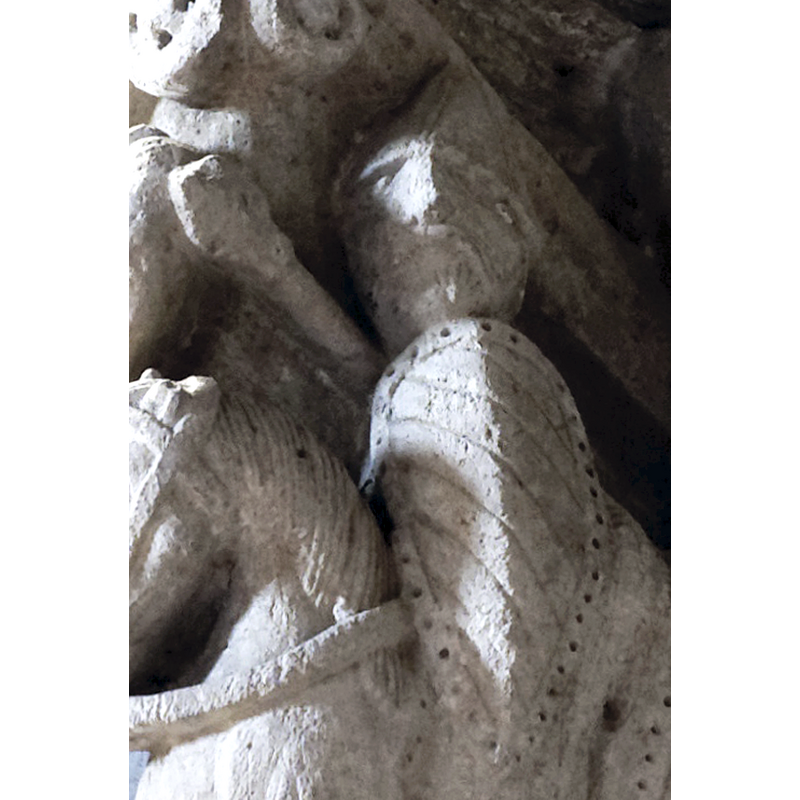 capital on the north side of the chancel arch: on the left side of the capital is a mounted male holding an object and/with a flowing cloth in the right hand; the left hand hold the bridle and a ring, or the ring is secured to the saddle; the horse tramples over a fallen bearded man who appears unarmed; the front side of the capital has a balcony with two males in it looking out; below the balcony a male figure leans on a short pillar (to which he may be tied?); the right side of the capital has a bearded man loading a stone into his sling, by the side of a mounted knight armed with a lance and a shield, and wearing a helmet; behind him is an unidentified beast