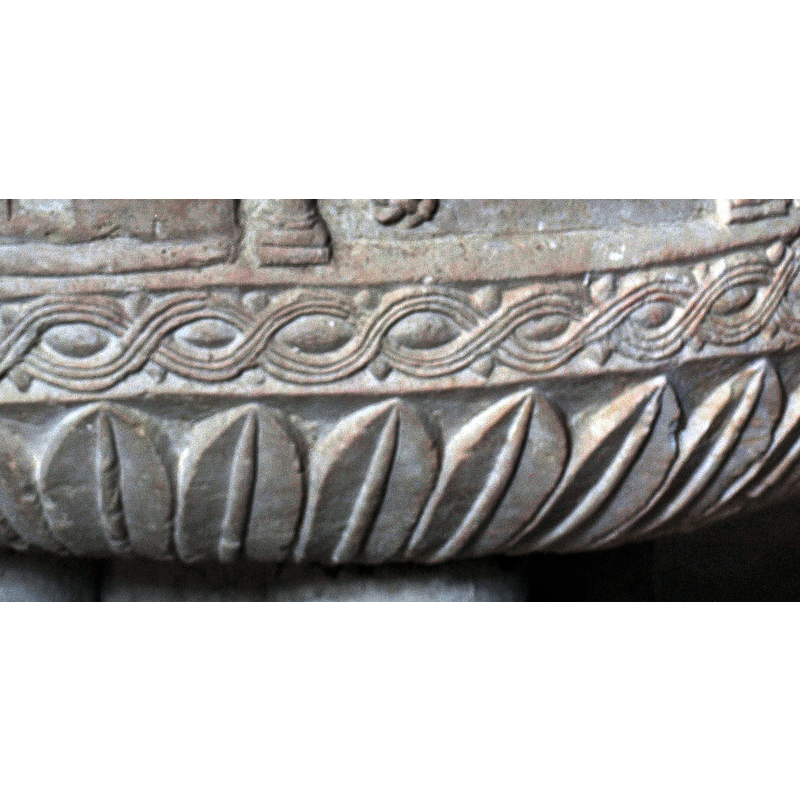 with pellet motif in the spandrels of the braid; all around except where the three-head motif protrudes [cf. FontNotes]