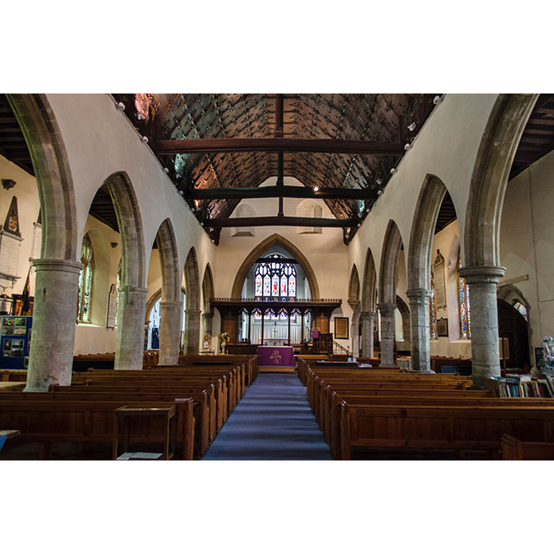 the top of the font is discernible on the right side of the image, between two pillars of the south colonnade, by the south entranceway -- Photo caption: "Grade I listed. 14th to 15th Century church. The chancel is Early English. The nave has a wooden ceiling. The tower dates from 1467 and is similar to Ashford and Lydd. There are two blocked windows above the chancel arch. Restored 1864."