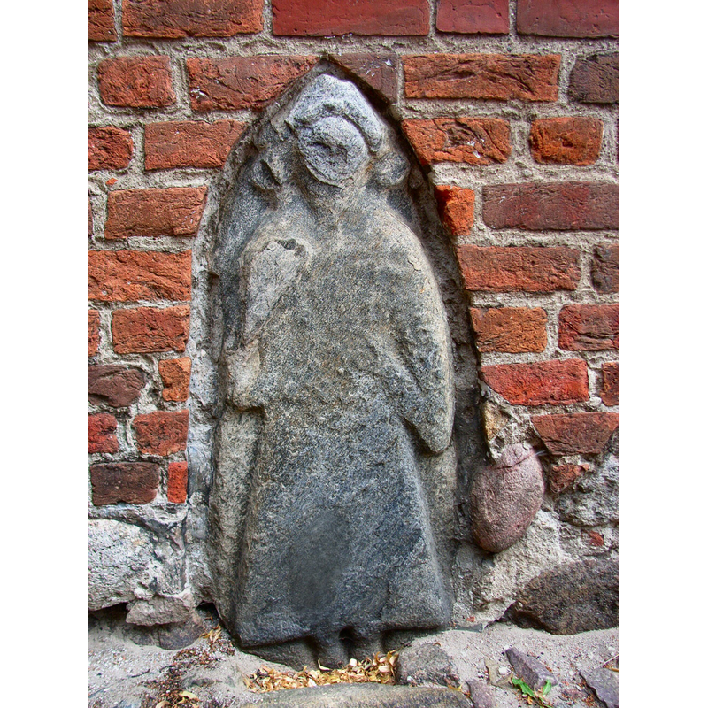 a statue embedded in the west brick wall of the church; perhaps a gravestone originally -- Photo caption: "Bildstein in der Westfassade der St. Marienkirche in Bergen auf Rügen. Alter, Herkunft und Bedeutung sind umstritten. Es ist anzunehmen, dass es sich entweder um den Grabstein des Fürsten Jaromar I. († um 1218) oder, ähnlich dem Svantevit-Stein in der Kirche von Altenkirchen auf der Halbinsel Wittow, eher um das Abbild eines Priesters des slawischen Svantevit-Tempels am Kap Arkona aus der Zeit vor 1168 handelt. Der Stein ist offenbar nachträglich bearbeitet worden: Dort, wo die Figur auf dem Svantevit-Stein von Altenkirchen ein großes Trinkhorn trägt, ist hier (bei einer Ansicht von der Seite) in einer breiten Vertiefung die Andeutung eines Kreuzes zu erkennen."