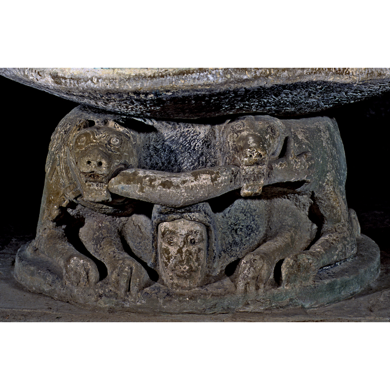One of two lions that make up the base; this one chained, holding a human arm in its jaws