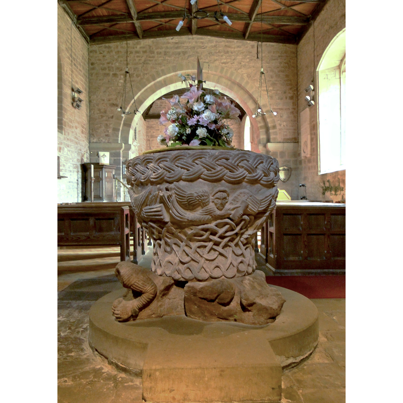 the font seen from the west end of the nave -- source caption: "St Michael, Castle Frome. A small early Norman village church set below the almost invisible remains of an 11th century castle and containing this masterpiece, a late work of the Herefordshire School and possibly the finest example, although the good folk of Eardisley may not concur."