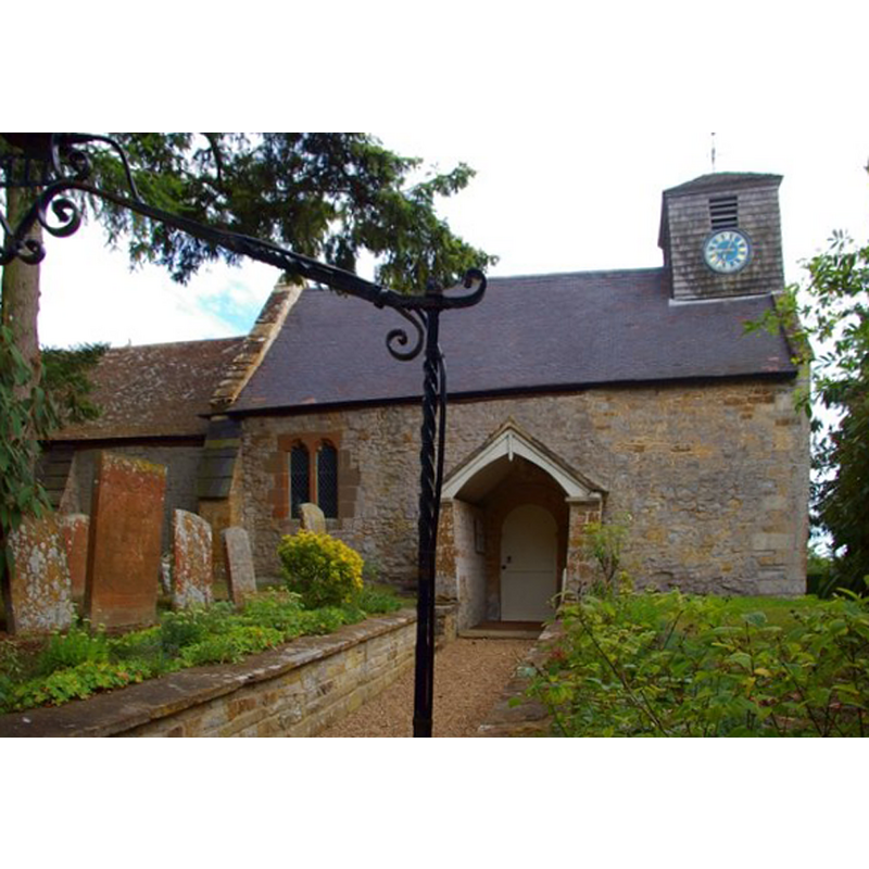 Source caption: "Church of St James the Great, Idlicote. The church, away from the village and in the grounds of the big house, was built of the local lias about 1200, as shown by the round Norman doorway within the later Georgian porch. The shingled bellcote and clock were added in the 1960s."