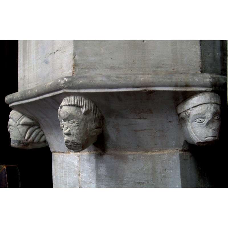 three of the heads on the underbowl: the left is male, with a broken nose, and have had a dark-coloured beard; the one in the centre resembles those intended to appear negroid in medieval font art; the head on the right is female, has a broken nose, and wears a wimple