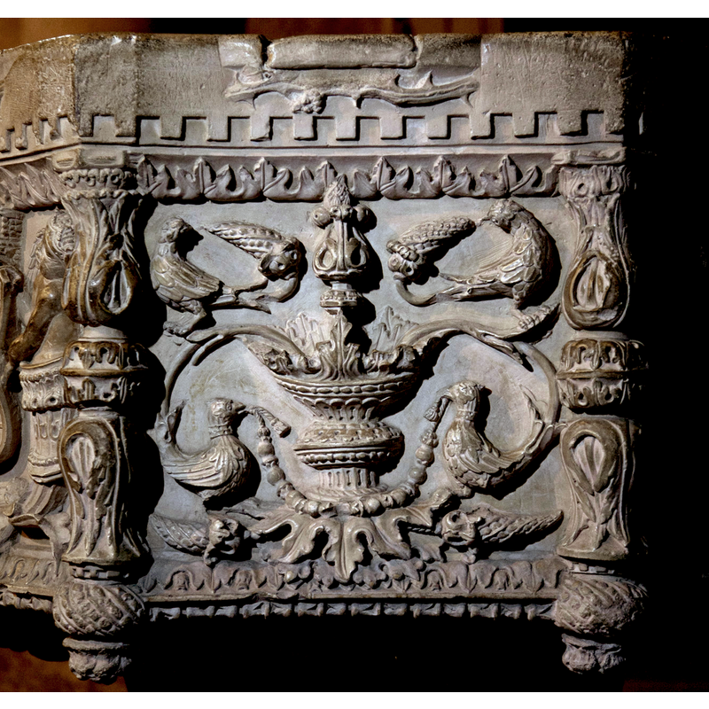 a very ornate arrangement involving two pheasants and two other birds, a central fountain and four ears of corn; the tails of the pheasants are connected to flowers issuing from the fountain; the two upper birds pick at the corn, but the lower birds do not, as their beaks hold a garland...