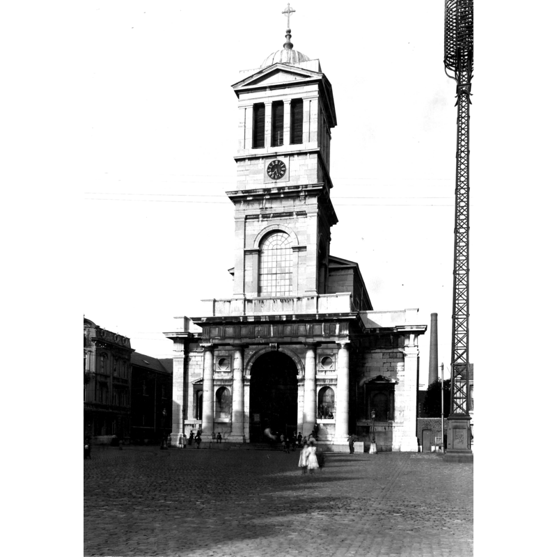 the modern church -- Source caption: "Le sanctuaire actuel est l'oeuvre de l'architecte Jean-Pierre Cremer, d'Aix-la-Chapelle, dont les plans "revus" par Louis-Hippolyte Lebas, de Paris, ont été mis en chantier sous la conduite des architectes verviétois Jacques Vivroux et son fils Auguste-Marie Vivroux. La première pierre fut posée le 22 septembre 1834 et la cérémonie de la consécration se déroula le 8 octobre 1838. Edifice néo-classique avec façade monumentale écrasée par la tour carrée centrale, en pierre, et long vaissseau se terminant par une abside semi-circulaire, en brique. L'intérieur scandé de piliers toscans et couvert dans la large nef principale de plafonds à caissons donne une impression d'équilibre et de majesté."
